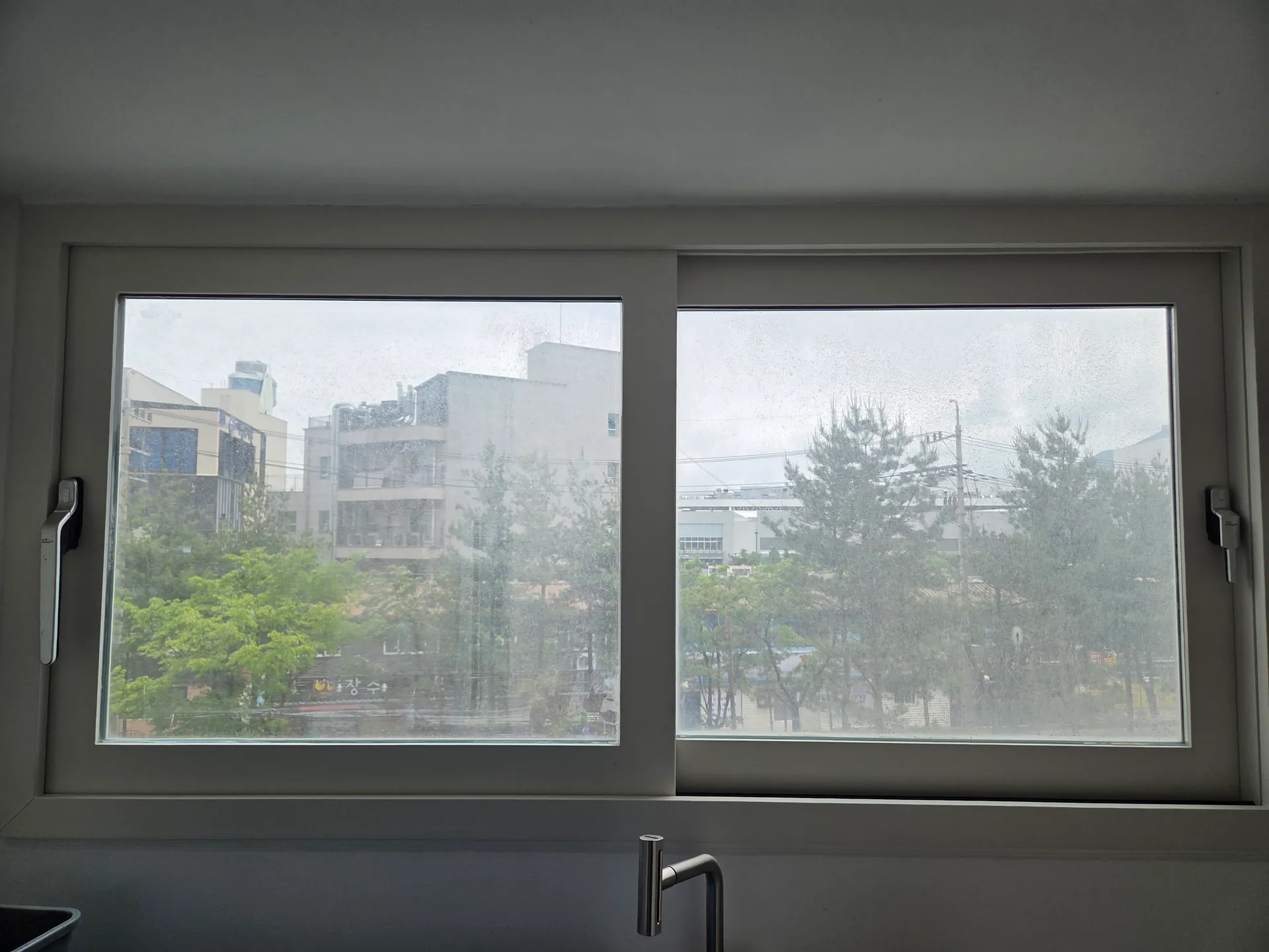 완료한 베란다 미닫이창 너머 난간과 단지 건물, 나무가 이어지는 전경