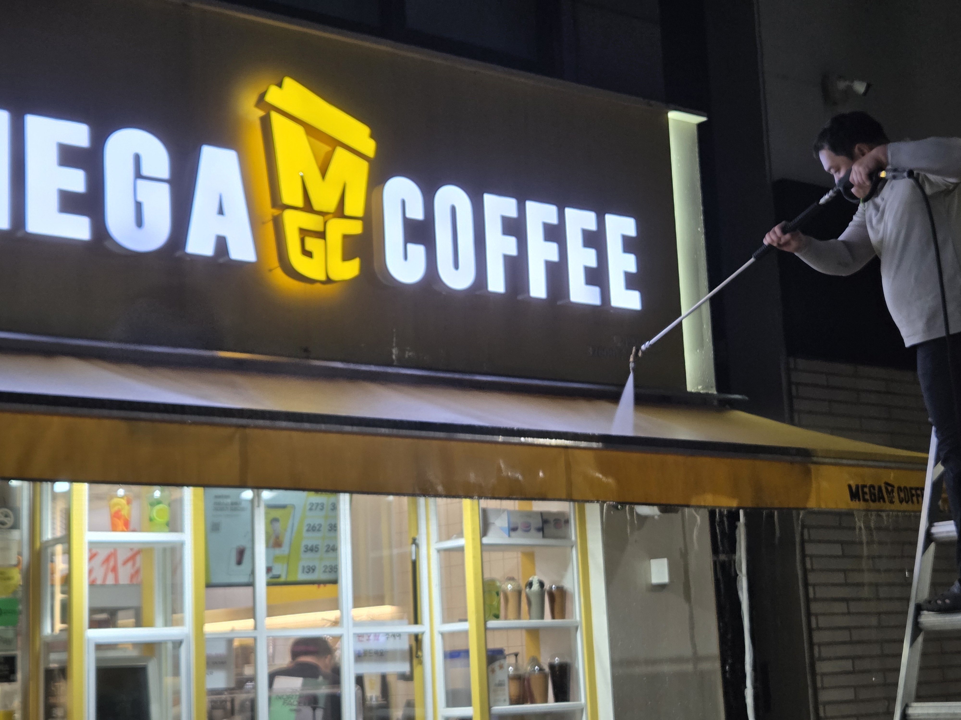 베이지색 매장 어닝 표면을 브러시로 청소하는 작업자